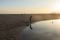 Junge am Strand, Blick auf sein Spiegelbild in einem Wasserbecken, Ebbe, Sonnenuntergang. — Stockfoto