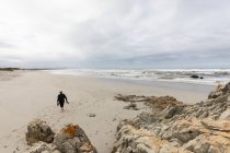 Ein reifer Mann, der mit seinen Schuhen in der Hand über einen Strand läuft — Stockfoto
