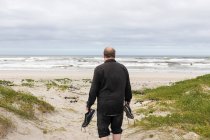Um homem maduro andando através de uma praia carregando seus sapatos em sua mão — Fotografia de Stock