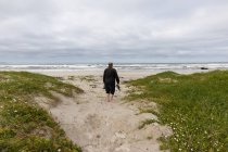 Un hombre maduro caminando por una playa llevando sus zapatos en la mano - foto de stock