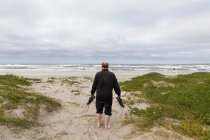 Ein reifer Mann, der mit seinen Schuhen in der Hand über einen Strand läuft — Stockfoto
