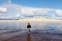 A teenage girl wading through a water channel on a wide sandy beach. — Stock Photo