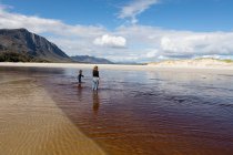 Teenage girl and young boy on an open sandy beach wading through shallow water. — Stock Photo