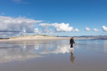 Un homme adulte portant un chapeau marchant le long d'une plage de sable. — Photo de stock