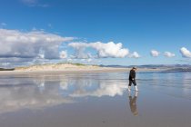 Un hombre adulto con un sombrero caminando por una playa de arena. - foto de stock