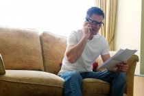 Homem sentado no sofá fazendo telefonema segurando papelada. — Fotografia de Stock