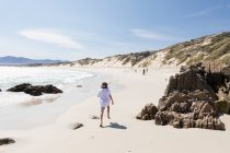Niño de ocho años explorando una amplia playa de arena. - foto de stock