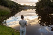 Teenage girl standing by a river at dusk. — Stock Photo