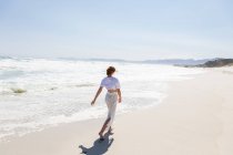 Adolescente caminando en una playa de arena en el borde del agua - foto de stock