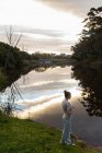 Adolescente debout près d'une rivière au crépuscule. — Photo de stock