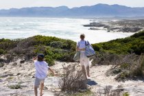 Adolescente et jeune frère surplombant une plage et une côte rocheuse avec des vagues s'écrasant sur le rivage. — Photo de stock
