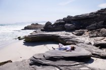 Adolescente deitada de costas em rochas acima de uma praia de areia. — Fotografia de Stock