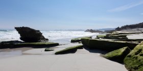 Скалы и скалы с видом на песчаный пляж с волнами, разбивающимися о берег — стоковое фото