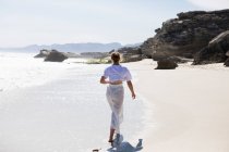 Teenage girl walking on a sandy beach at the water's edge — Stockfoto