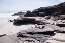 Adolescente couchée sur le dos sur des rochers au-dessus d'une plage de sable. — Photo de stock