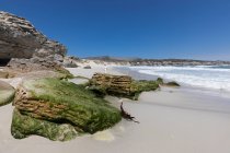 Formaciones rocosas y acantilados con vistas a una playa de arena con olas rompiendo en la orilla - foto de stock