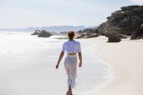 Teenage girl walking on a sandy beach at the water's edge — Stockfoto