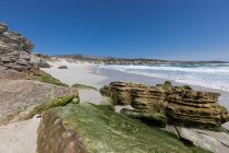 Скельні утворення та скелі з видом на піщаний пляж з хвилями, що ламаються на березі — стокове фото
