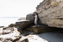Teenage girl exploring the cliffs and rock strata on a beach on the Atlantic shore. — Stock Photo