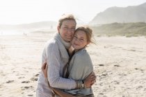Mulher adulta e sua filha adolescente abraçando, de pé em uma praia varrida pelo vento — Fotografia de Stock
