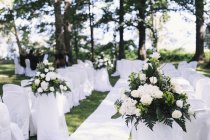 A garden with tables laid under the shade of tall trees, set for a wedding — Stock Photo