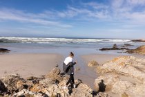 Adolescente de pé sobre rochas com vista para uma praia de areia — Fotografia de Stock
