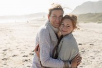 Mulher adulta e sua filha adolescente abraçando, de pé em uma praia varrida pelo vento — Fotografia de Stock