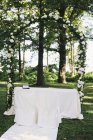 Сад со столами, накрытыми в тени высоких деревьев, цветочная арка, обстановка для свадьбы — стоковое фото
