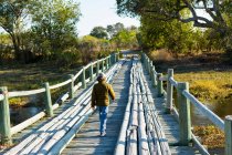 Un garçon traversant seul un pont en bois sur un marais — Photo de stock