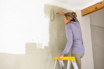 Una mujer decorando una habitación, pintando paredes. - foto de stock