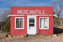 A red painted building frontage, with a sign MERCANTILE, windows boarded up. — Stock Photo