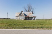 Casa abandonada com um telhado de estanho enferrujado em terras agrícolas por uma estrada. — Fotografia de Stock