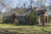 Una casa rural o pequeña casa abandonada y desmoronada, cubierta de plantas y arbustos. - foto de stock
