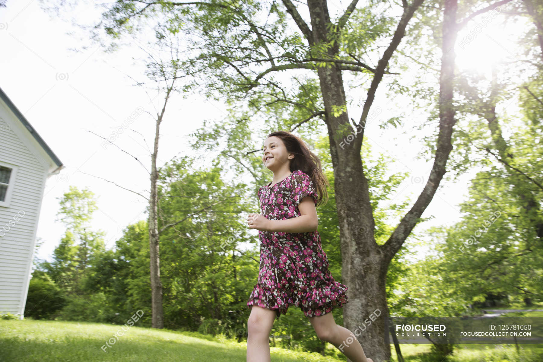 Girl running across grass — horizontal, lens flare Stock Photo