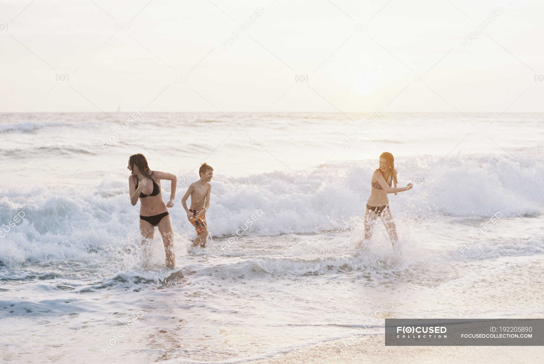 Teenage Girls And Pre Teen Boy Playing On Sandy Beach By Ocean Activity Bikini Stock Photo
