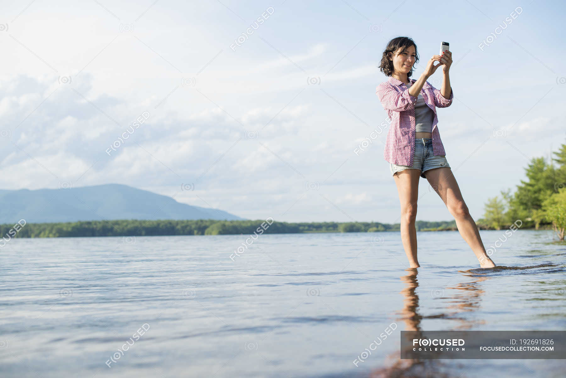 Woman standing in lake water and taking picture with smartphone ...