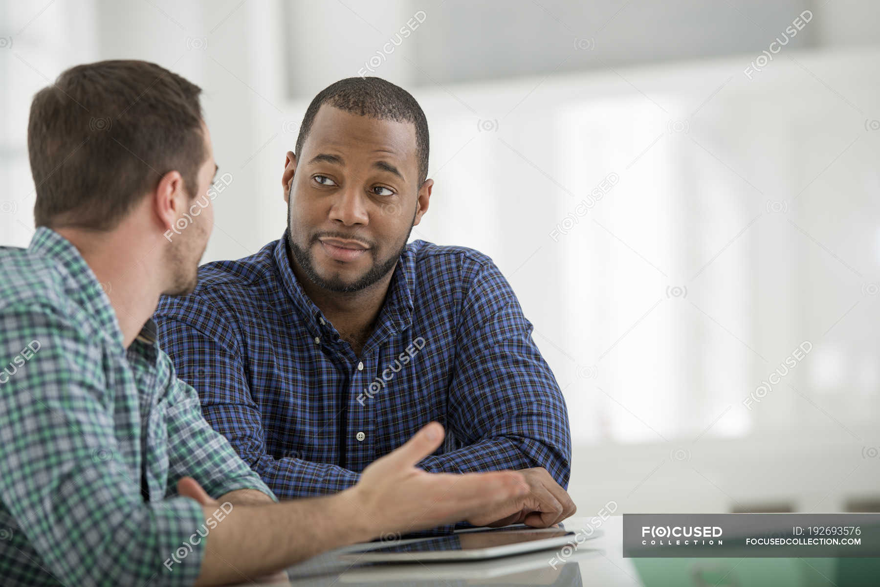 two-men-sitting-at-table-with-digital-tablet-and-talking-in-office