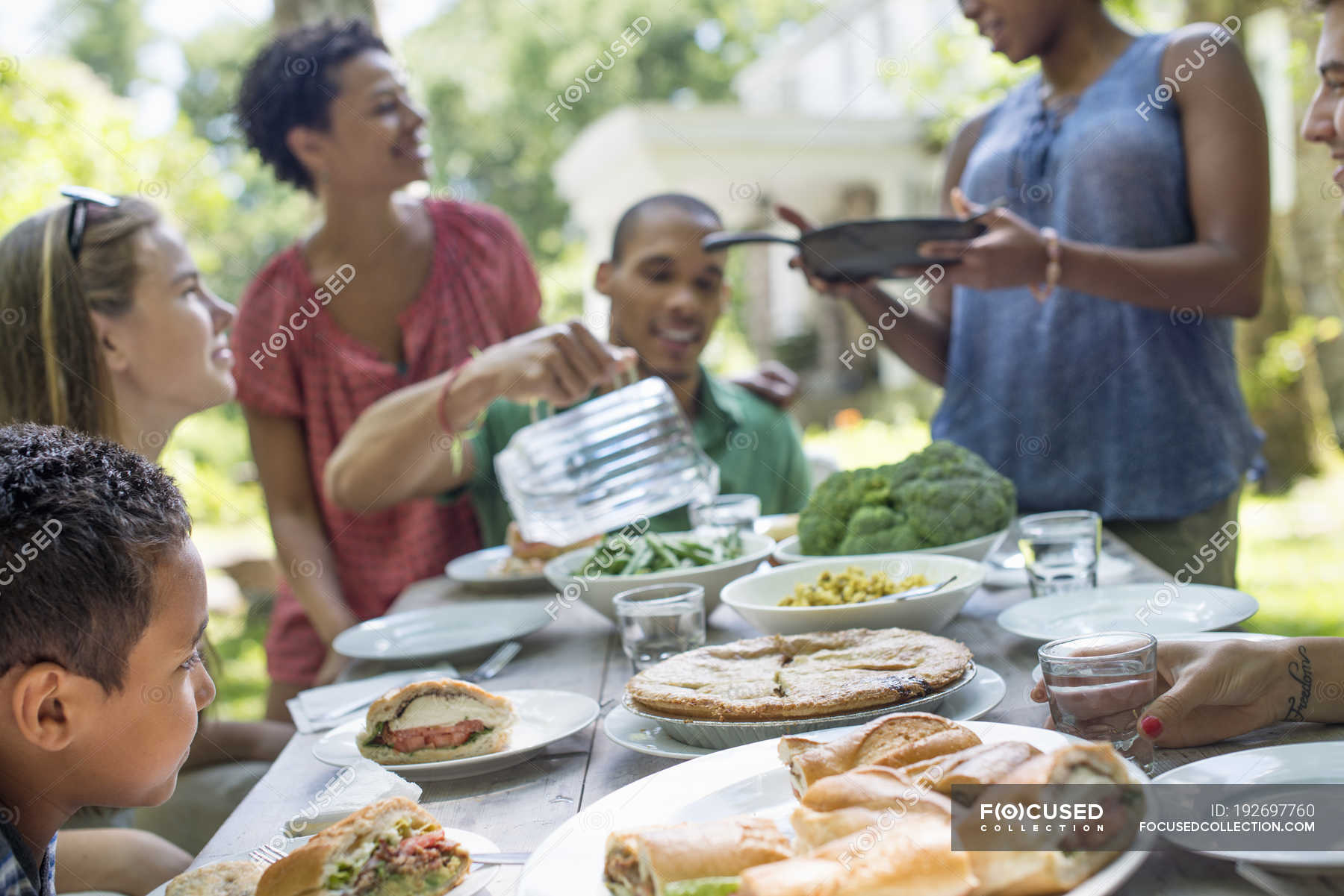 Friends And Family Gathering Around Dinner Table In Countryside Garden Female