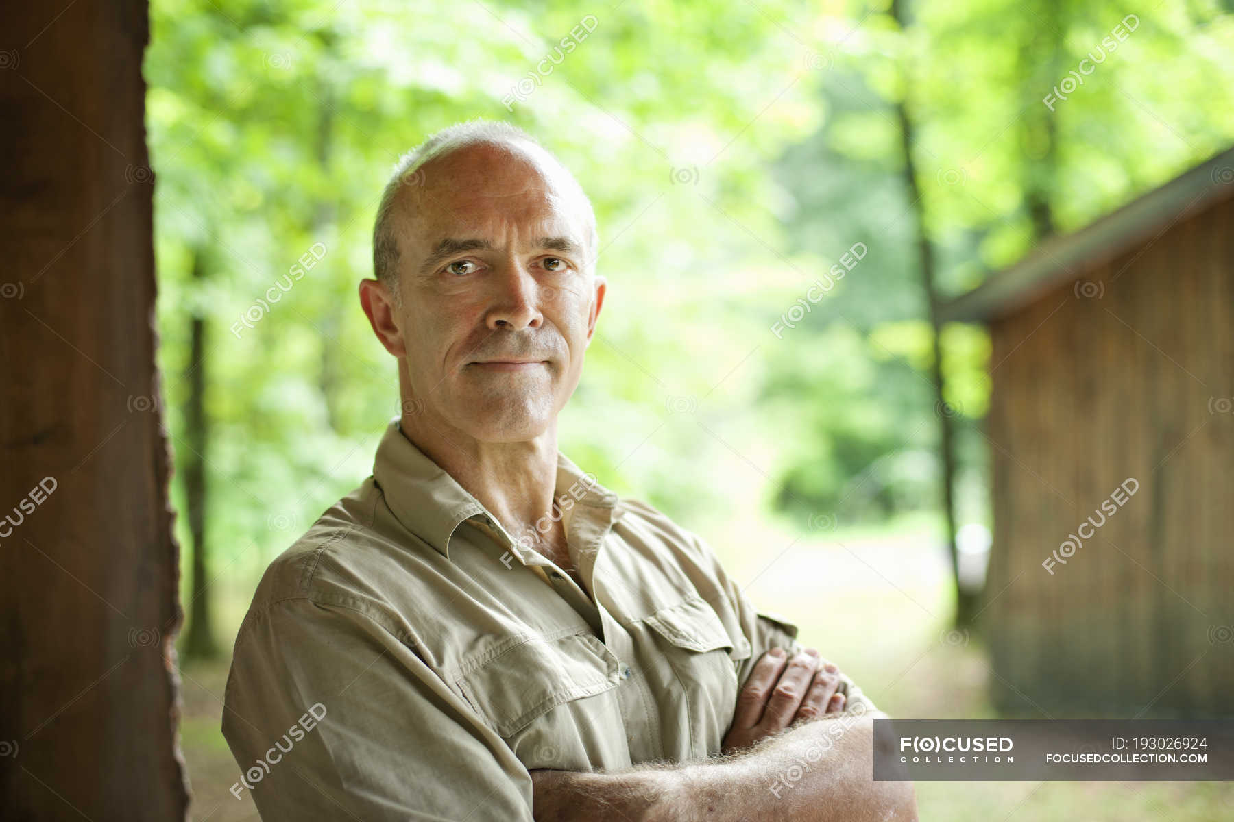 Mature man standing with arms crossed in front of wooden hut in ...