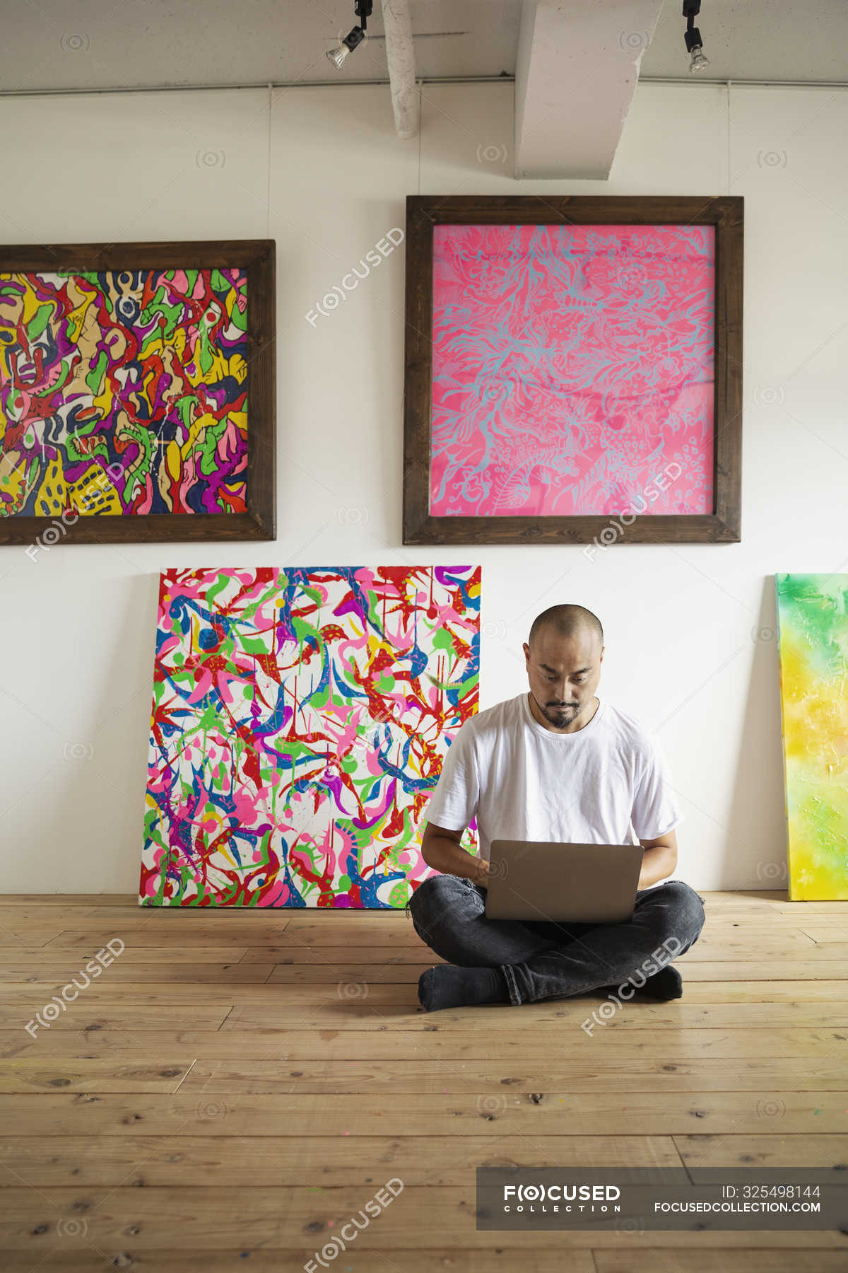 Japanese Man Sitting On Floor Of Art Gallery Working On Laptop