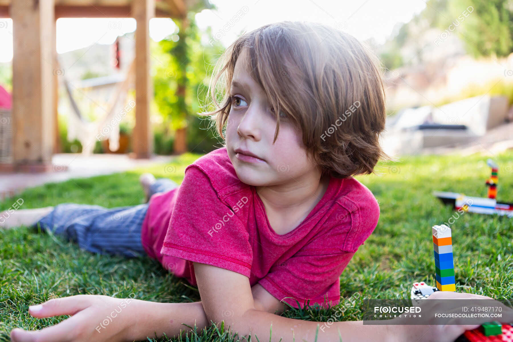 Boy with brown hair lying on lawn, playing with building blocks. — day ...