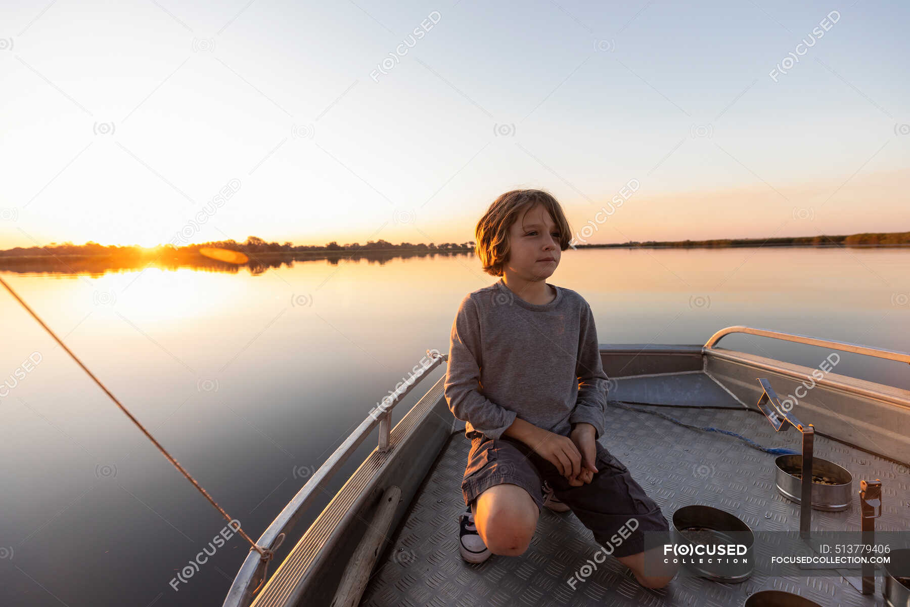 A young boy fishing from a boat on the flat calm waters of the Okavango ...