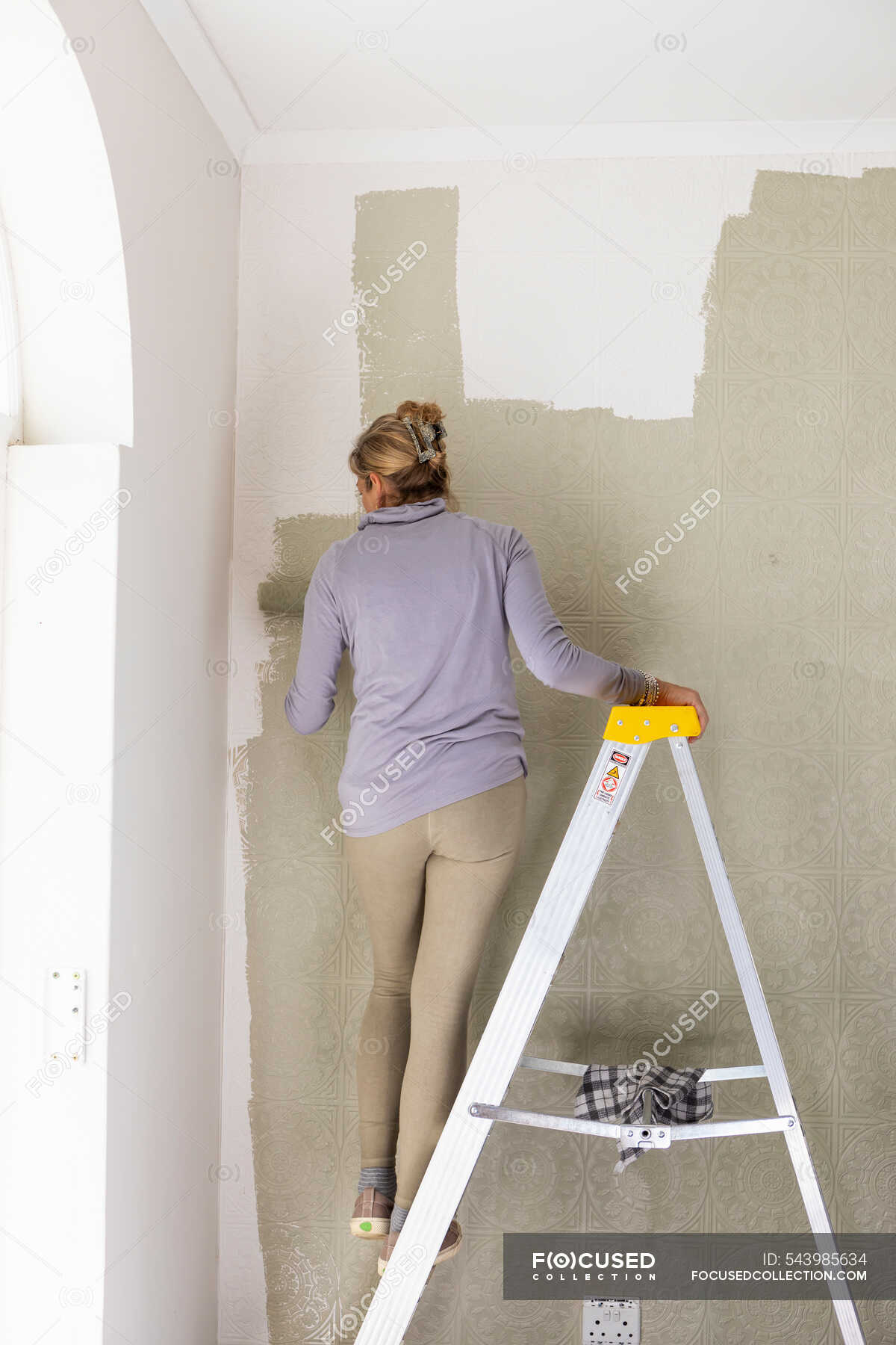 A woman on a ladder using a paint roller, decorating a room — women