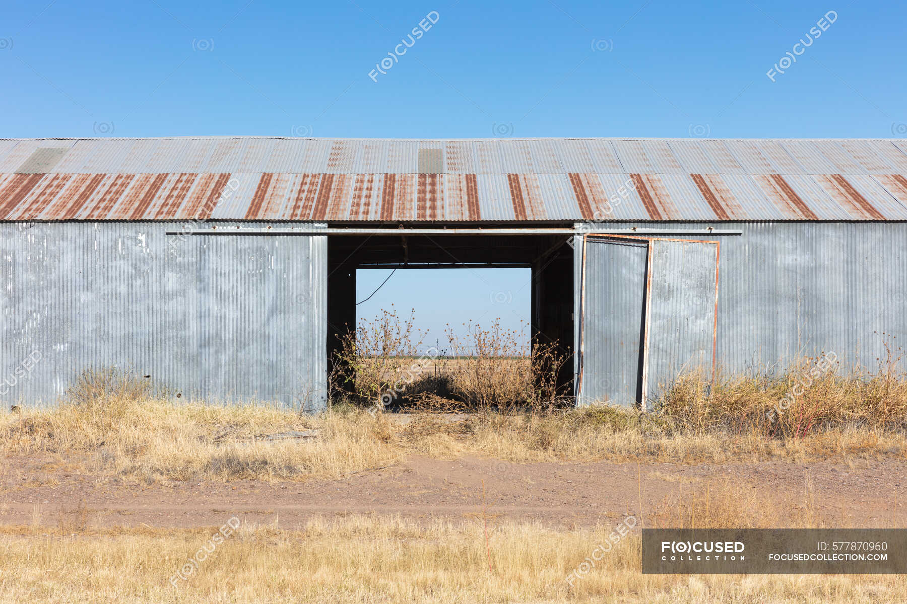 Abandoned rusting metal farm building with large open doors. — Texas