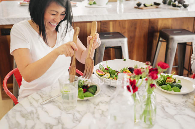 Жінка використовує сервери для салату, щоб завантажити свою тарілку — стокове фото