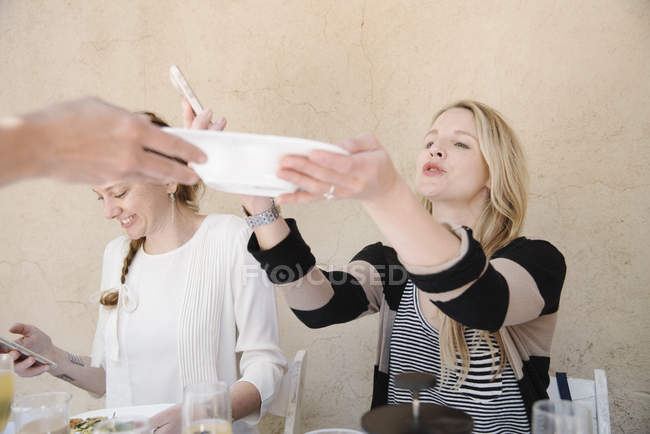 Women one reaching for a plate of food. — Stock Photo