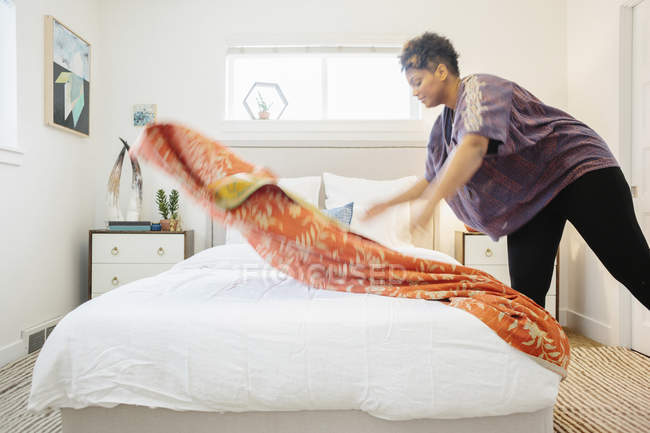 Женщина, расстилающая одеяло с цветочным узором на двуспальной кровати — стоковое фото
