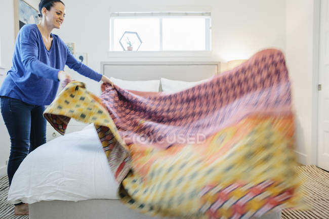 Mulher espalhando uma colcha estampada colorida sobre — Fotografia de Stock
