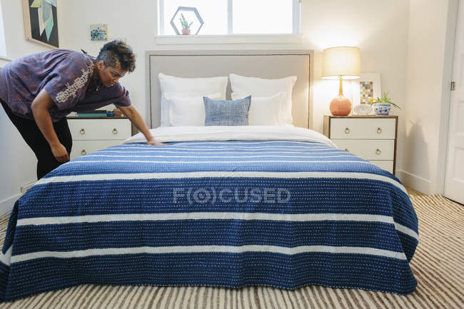 Woman smoothing a blue striped throw over — Stock Photo