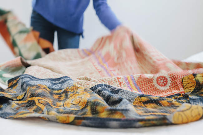 Femme écartant une courtepointe de tissu sur un lit — Photo de stock